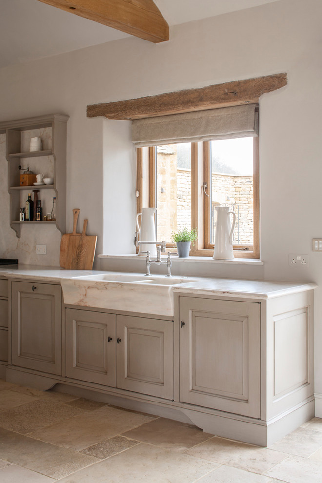 Photo of a large traditional galley open plan kitchen in Gloucestershire with raised-panel cabinets, marble benchtops, white splashback, stone slab splashback, stainless steel appliances, limestone floors, with island, a double-bowl sink and beige cabinets.