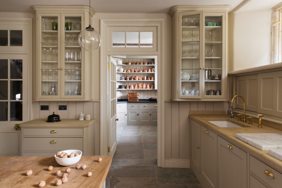 This is an example of a traditional galley separate kitchen in London with an undermount sink, shaker cabinets, beige cabinets, wood benchtops, beige splashback, timber splashback, coloured appliances, with island and grey floor.