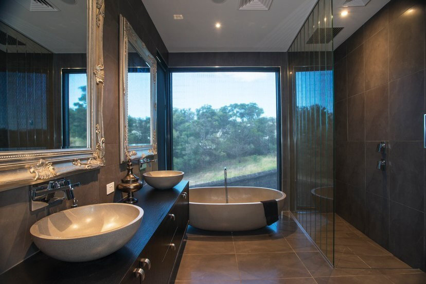 Modern inredning av ett stort brun brunt badrum, med skåp i mörkt trä, ett fristående badkar, en öppen dusch, grå kakel, grå väggar, ett fristående handfat, träbänkskiva, grått golv och med dusch som är öppen