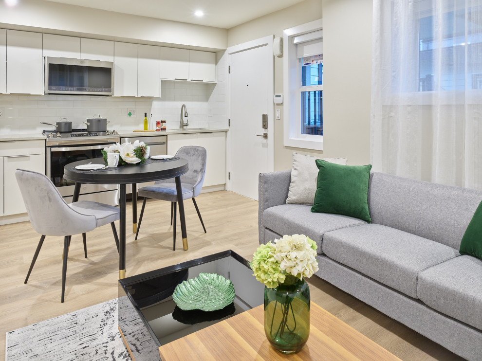 Example of a small transitional single-wall laminate floor and beige floor eat-in kitchen design in Vancouver with an undermount sink, flat-panel cabinets, white cabinets, quartzite countertops, white backsplash, ceramic backsplash, stainless steel appliances, an island and beige countertops