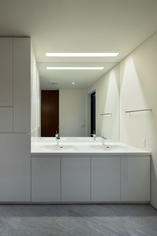 Example of a mid-sized minimalist white tile porcelain tile and gray floor powder room design in Fukuoka with flat-panel cabinets, white cabinets, white walls, an integrated sink, solid surface countertops, white countertops and a built-in vanity