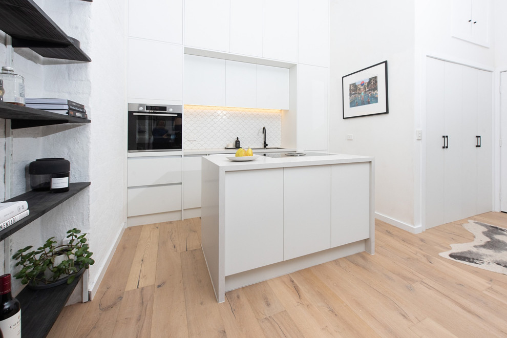Inspiration for a mid-sized modern u-shaped kitchen pantry in Melbourne with a drop-in sink, open cabinets, white cabinets, solid surface benchtops, white splashback, mosaic tile splashback, stainless steel appliances, with island, beige floor, medium hardwood floors and white benchtop.