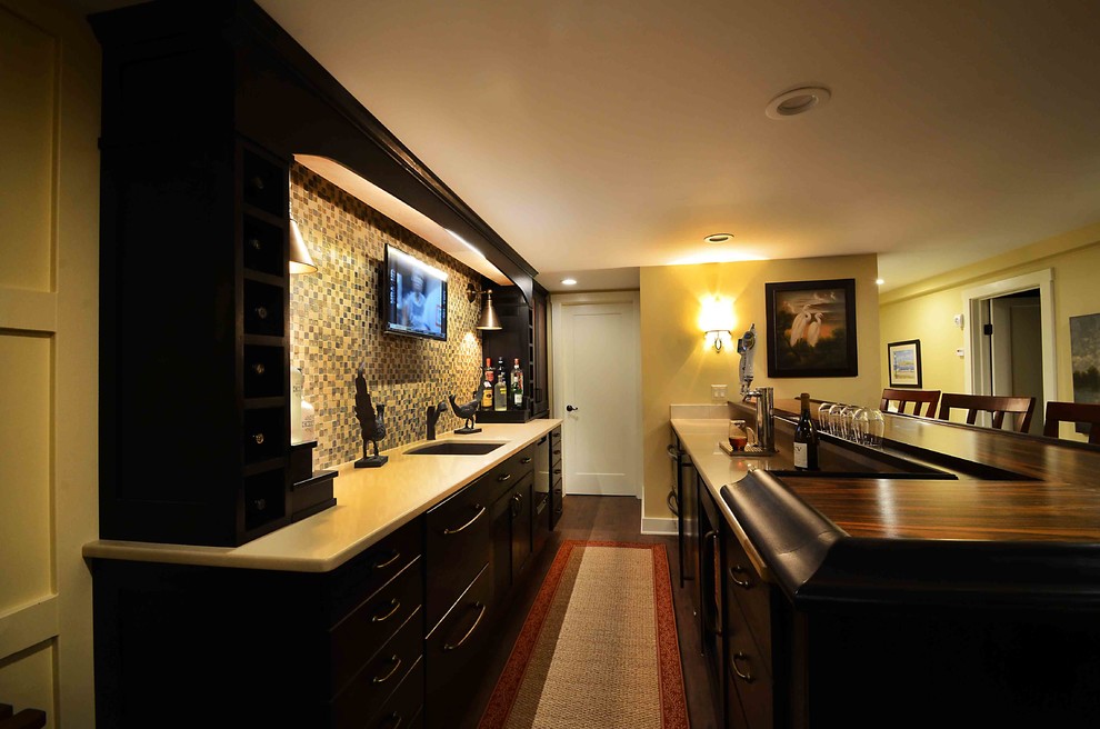 Design ideas for a mid-sized transitional galley seated home bar in New York with an undermount sink, flat-panel cabinets, black cabinets, limestone benchtops, beige splashback, stone tile splashback, dark hardwood floors and brown floor.