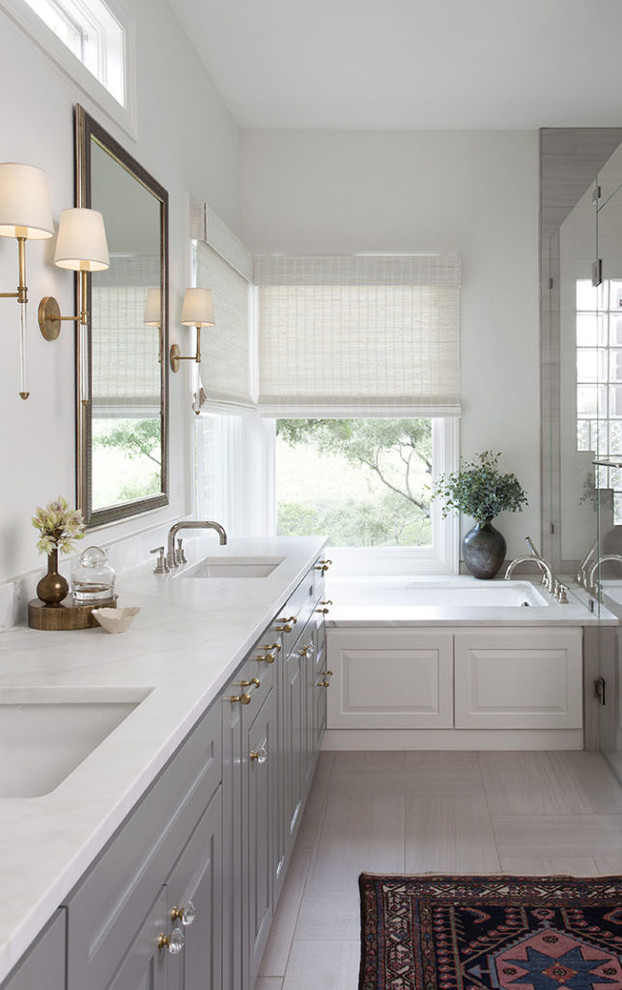 Design ideas for a large transitional master bathroom in Austin with raised-panel cabinets, grey cabinets, an undermount tub, an alcove shower, beige tile, porcelain tile, beige walls, porcelain floors, an undermount sink, marble benchtops, beige floor, a hinged shower door and white benchtops.