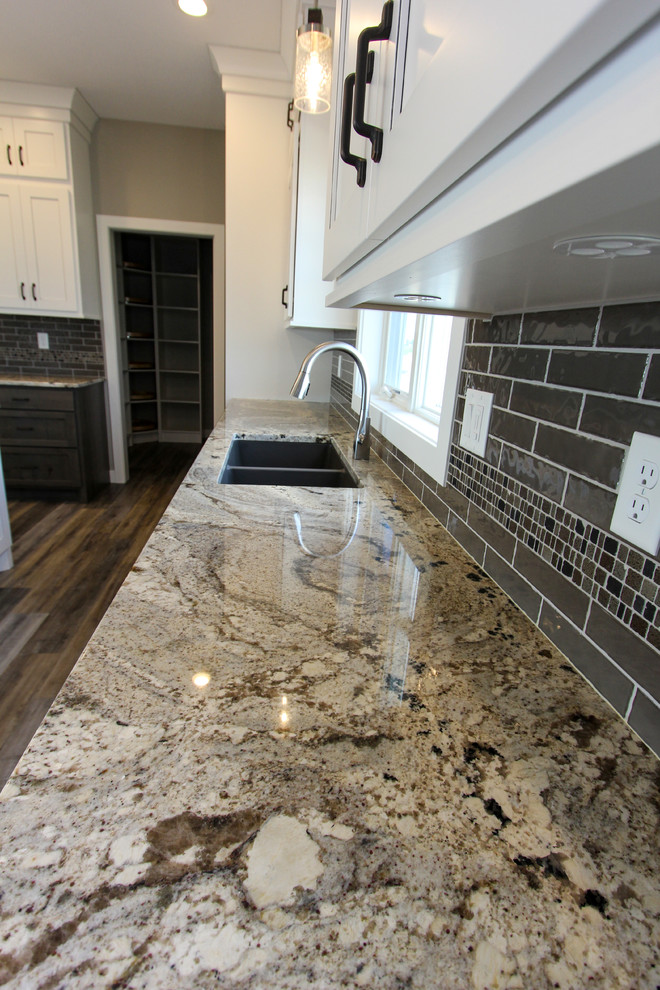 Mid-sized transitional l-shaped laminate floor and brown floor eat-in kitchen photo in Minneapolis with an undermount sink, shaker cabinets, white cabinets, granite countertops, gray backsplash, ceramic backsplash, an island and multicolored countertops