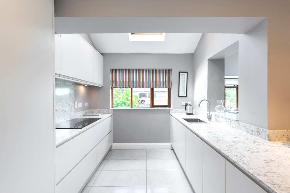 Mid-sized contemporary galley open plan kitchen in Dublin with a drop-in sink, glass-front cabinets, grey cabinets, quartzite benchtops, grey splashback, engineered quartz splashback, panelled appliances, porcelain floors, a peninsula, grey floor and grey benchtop.