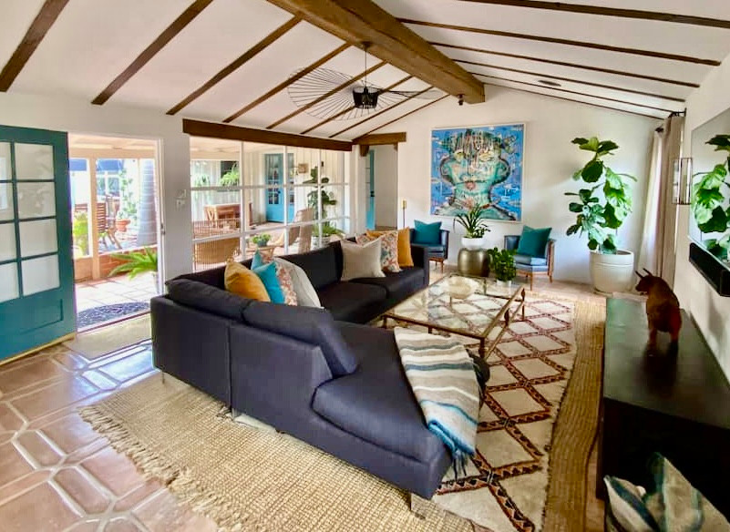 Large mediterranean open concept living room in San Diego with a corner fireplace, a plaster fireplace surround, a wall-mounted tv, orange floor and exposed beam.