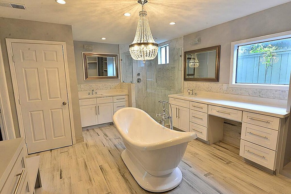 Photo of a mid-sized transitional master bathroom in Houston with shaker cabinets, white cabinets, a freestanding tub, a corner shower, a one-piece toilet, grey walls, an undermount sink, quartzite benchtops, grey floor, a hinged shower door, white tile, stone tile and vinyl floors.
