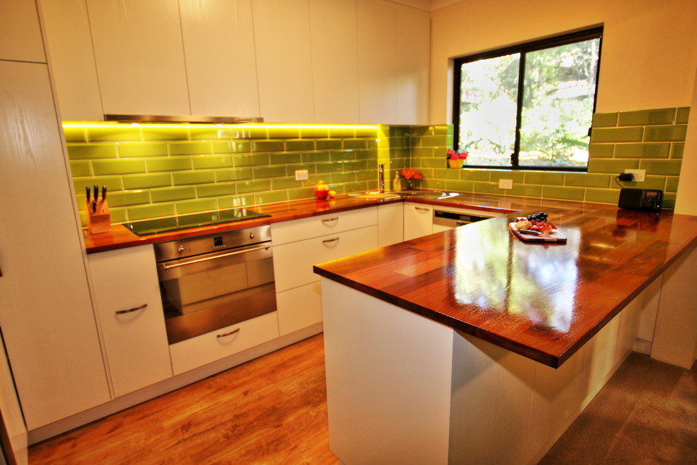 Inspiration for a small contemporary u-shaped eat-in kitchen in Sydney with a drop-in sink, flat-panel cabinets, light wood cabinets, wood benchtops, green splashback, subway tile splashback, stainless steel appliances, light hardwood floors and a peninsula.