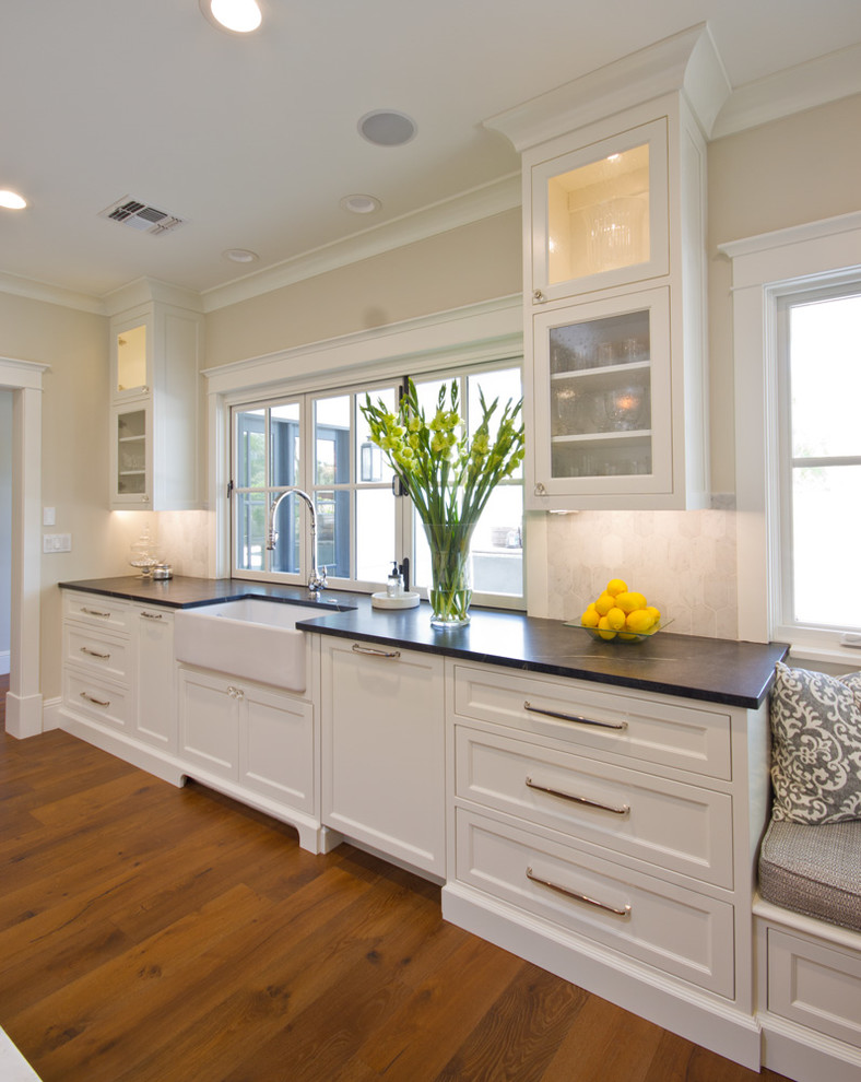 Inspiration for a large transitional u-shaped medium tone wood floor eat-in kitchen remodel in Phoenix with a farmhouse sink, recessed-panel cabinets, white cabinets, marble countertops, white backsplash, stone tile backsplash, stainless steel appliances and an island