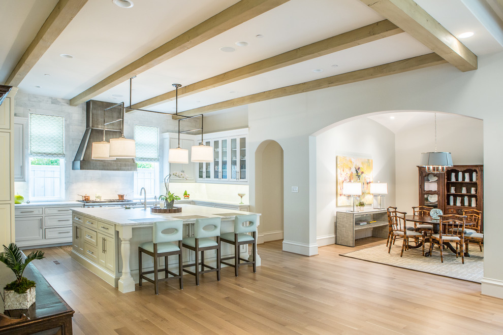 Example of a transitional l-shaped light wood floor open concept kitchen design in Dallas with an undermount sink, recessed-panel cabinets, white cabinets, marble countertops, white backsplash, stainless steel appliances and an island