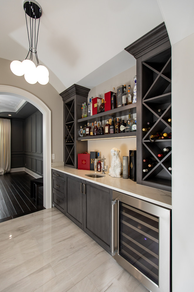 This is an example of a transitional single-wall home bar in Detroit with an undermount sink, shaker cabinets, dark wood cabinets and beige floor.