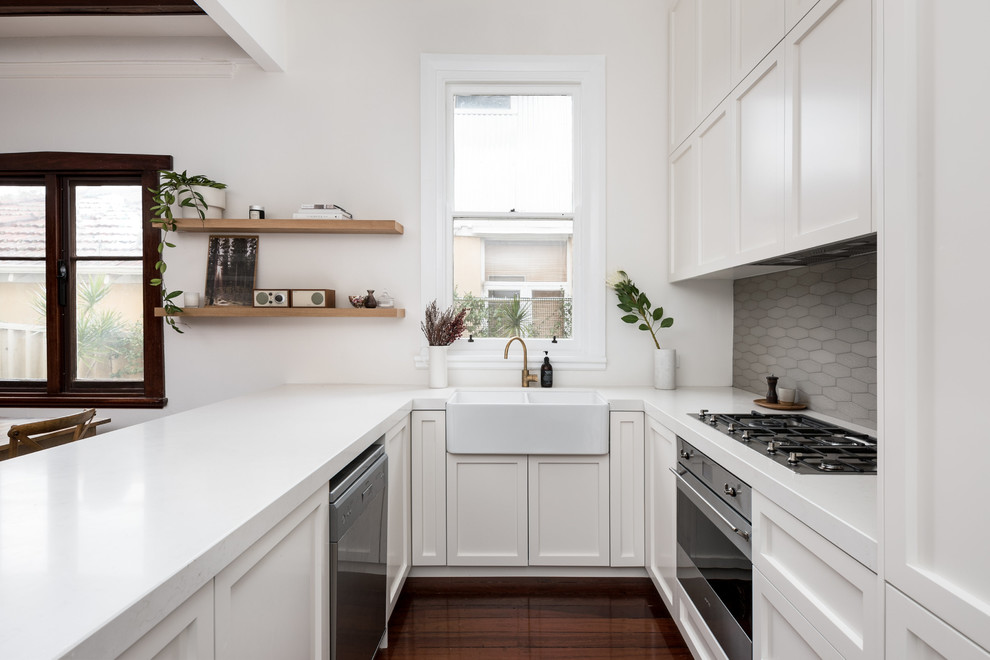 Mid-sized scandinavian u-shaped kitchen in Perth with a farmhouse sink, shaker cabinets, white cabinets, grey splashback, stainless steel appliances, dark hardwood floors, a peninsula and brown floor.