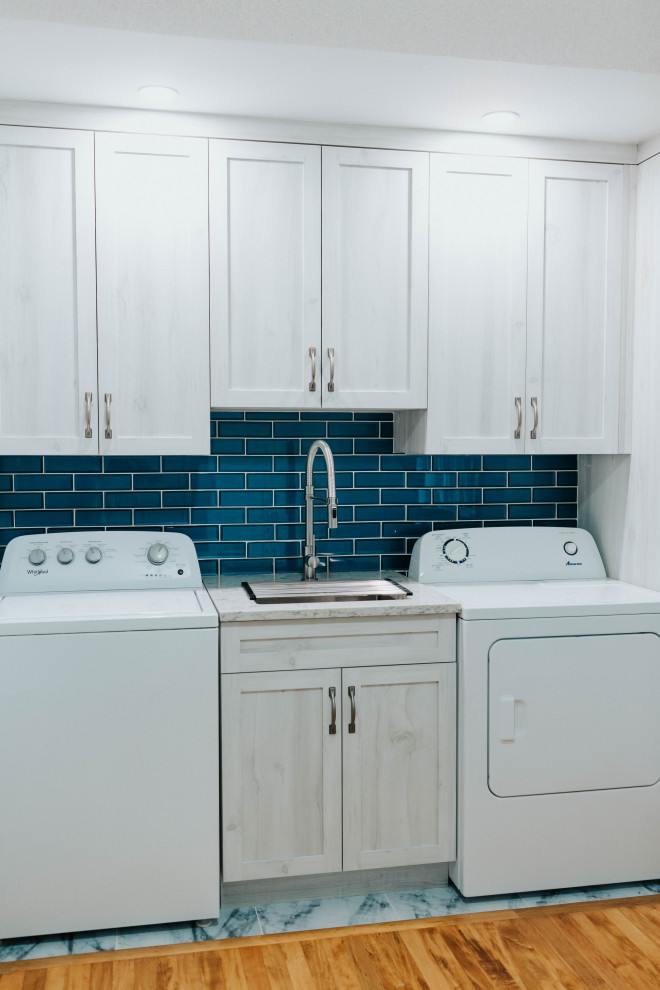 トロントにある高級な中くらいなトランジショナルスタイルのおしゃれな家事室 (アンダーカウンターシンク、シェーカースタイル扉のキャビネット、グレーのキャビネット、クオーツストーンカウンター、青いキッチンパネル、ガラスタイルのキッチンパネル、グレーの壁、無垢フローリング、左右配置の洗濯機・乾燥機、グレーのキッチンカウンター) の写真