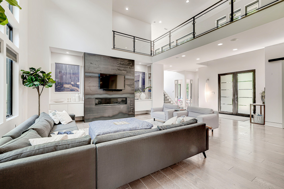 Photo of a large contemporary open concept living room in Indianapolis with white walls, light hardwood floors, a standard fireplace, a tile fireplace surround, a wall-mounted tv and grey floor.