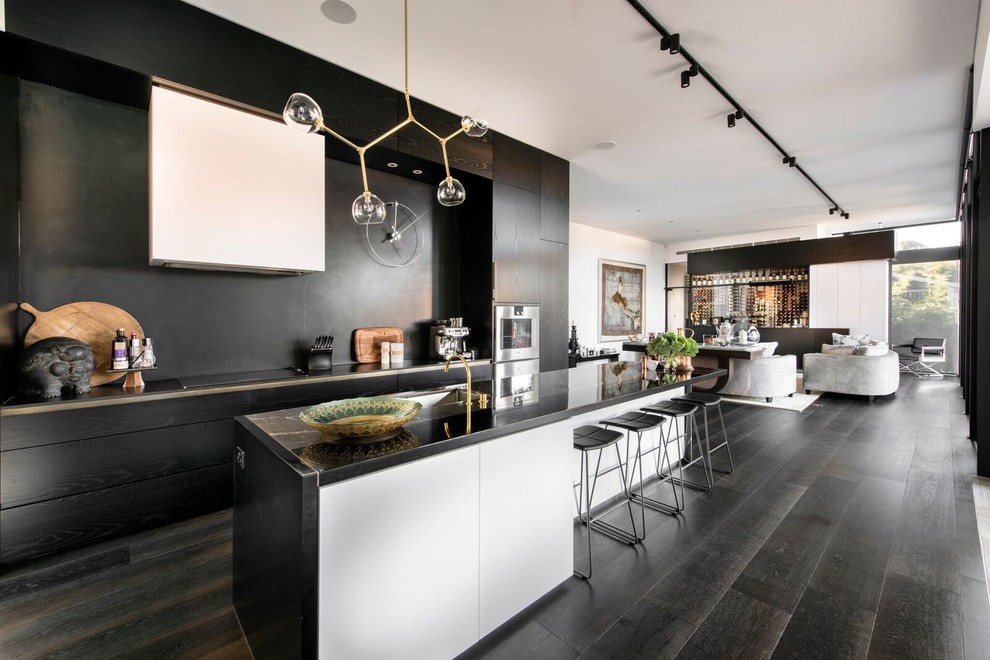 Design ideas for a contemporary galley open plan kitchen in Sunshine Coast with flat-panel cabinets, black splashback, stainless steel appliances, dark hardwood floors, with island and black floor.
