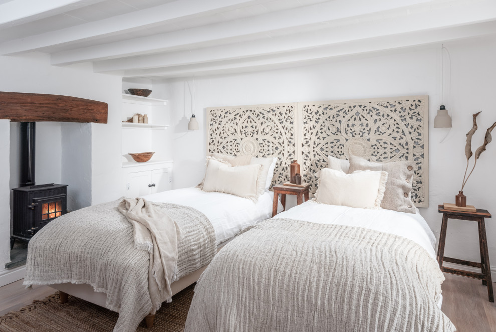 Cette photo montre une chambre d'amis bord de mer de taille moyenne avec un mur blanc, un sol en bois brun, une cheminée standard, un sol beige et poutres apparentes.