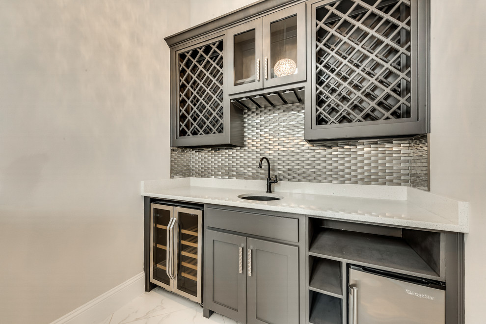 Photo of a large transitional u-shaped wet bar in Dallas with a drop-in sink, recessed-panel cabinets, grey cabinets, quartzite benchtops, grey splashback, metal splashback, marble floors, white floor and white benchtop.
