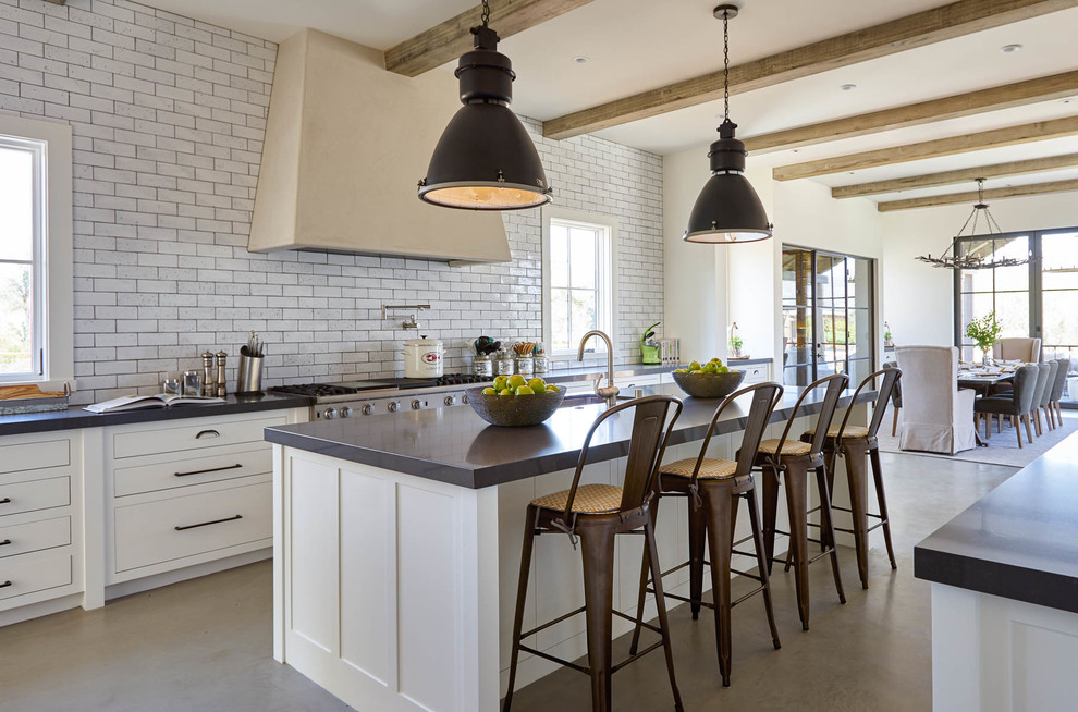 This is an example of a large country galley eat-in kitchen in San Francisco with flat-panel cabinets, white cabinets, grey splashback, with island, an undermount sink, quartz benchtops, subway tile splashback, stainless steel appliances, concrete floors and grey floor.