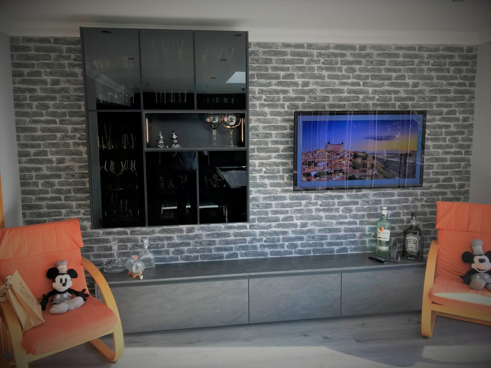 This is an example of a large modern l-shaped open plan kitchen in Sussex with a drop-in sink, flat-panel cabinets, grey cabinets, solid surface benchtops, orange splashback, glass sheet splashback, black appliances, with island and white benchtop.