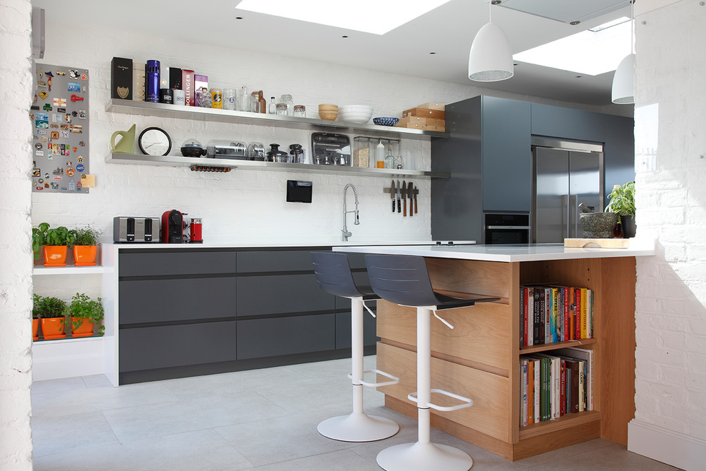 Photo of a contemporary kitchen in London with flat-panel cabinets, black cabinets, a peninsula, white splashback, brick splashback, stainless steel appliances, grey floor and white benchtop.