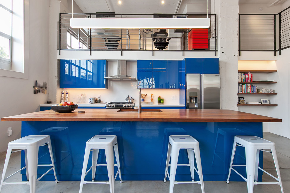 Urban concrete floor and gray floor kitchen photo in San Francisco with an undermount sink, flat-panel cabinets, blue cabinets, wood countertops, white backsplash, stainless steel appliances and an island