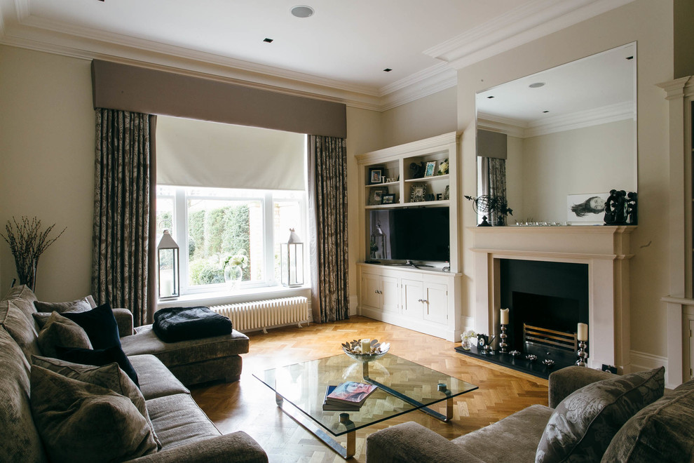 This is an example of a traditional family room in Cheshire with beige walls, medium hardwood floors, a standard fireplace and a freestanding tv.
