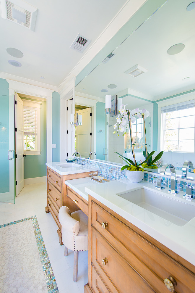 This is an example of a beach style master bathroom in Los Angeles with a drop-in sink, recessed-panel cabinets, medium wood cabinets, multi-coloured tile, blue walls and mosaic tile floors.