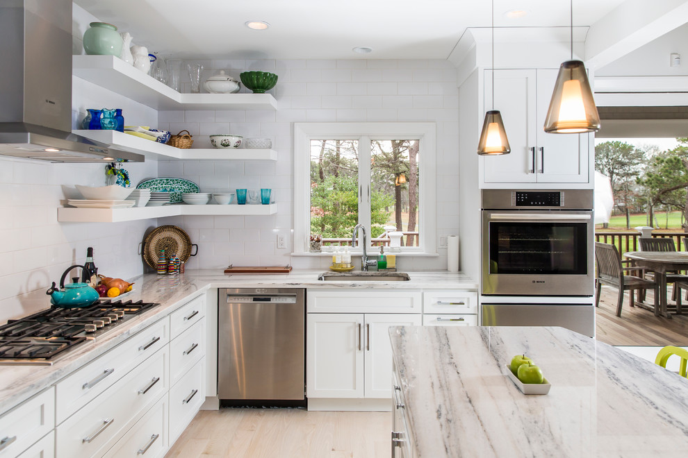This is an example of a transitional l-shaped eat-in kitchen in Boston with an undermount sink, shaker cabinets, white cabinets, white splashback, subway tile splashback, stainless steel appliances and with island.