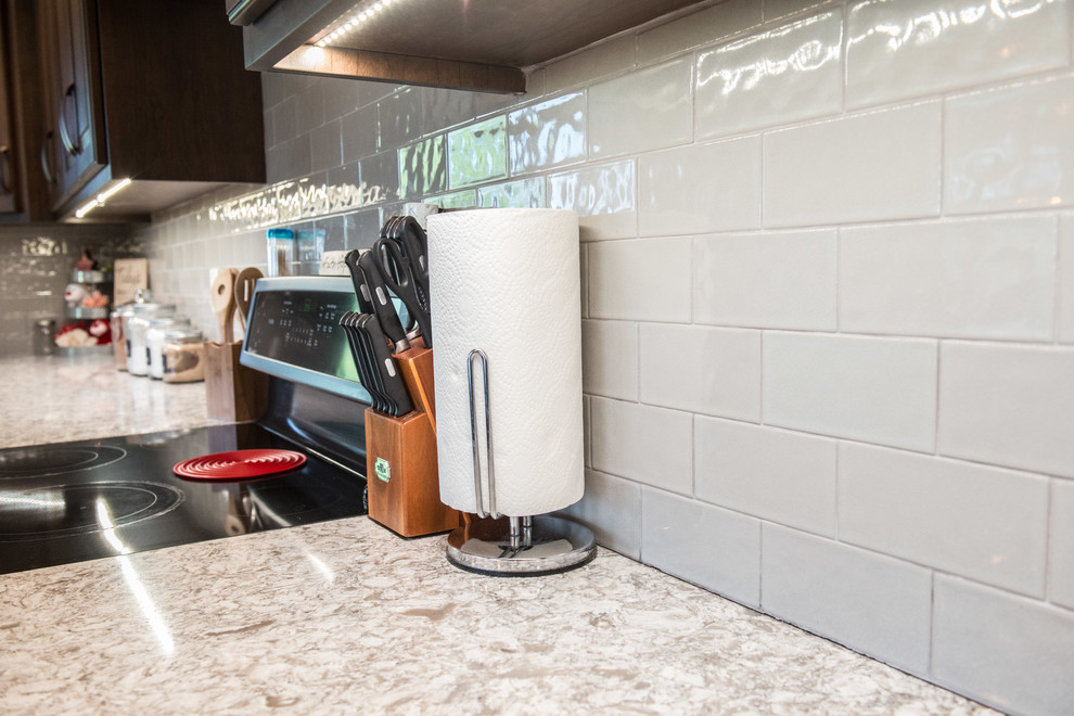 Huge transitional l-shaped medium tone wood floor home design photo with a farmhouse sink, raised-panel cabinets, medium tone wood cabinets, quartz countertops, gray backsplash, subway tile backsplash, stainless steel appliances, an island and multicolored countertops