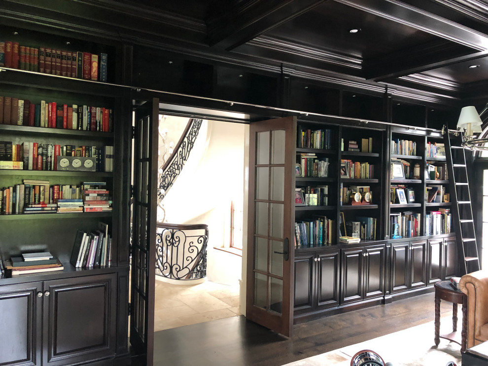 Photo of an expansive traditional home office in Chicago with a library, brown walls, dark hardwood floors, a standard fireplace, a wood fireplace surround, a freestanding desk and brown floor.