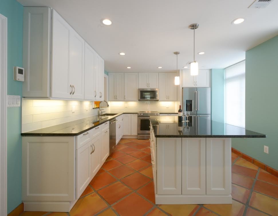 Mid-sized transitional l-shaped separate kitchen in DC Metro with an undermount sink, shaker cabinets, white cabinets, granite benchtops, white splashback, glass tile splashback, stainless steel appliances, terra-cotta floors, with island and brown floor.