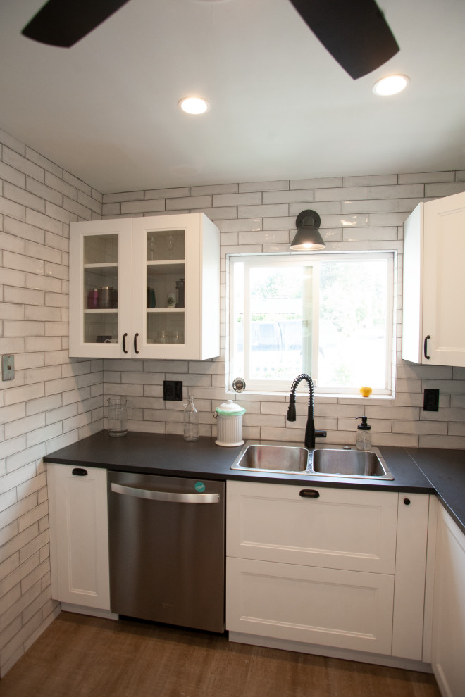 This is an example of a small contemporary u-shaped separate kitchen in Seattle with a double-bowl sink, recessed-panel cabinets, white cabinets, solid surface benchtops, grey splashback, subway tile splashback, stainless steel appliances, medium hardwood floors, no island, brown floor and black benchtop.