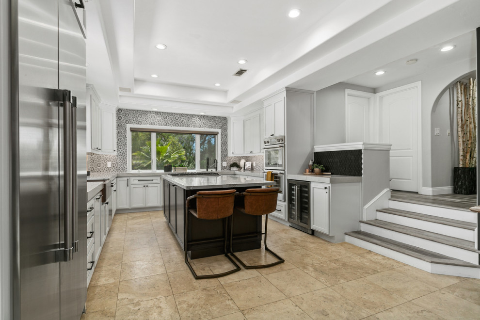 Bild på ett stort vintage grå grått kök, med en rustik diskho, skåp i shakerstil, grå skåp, marmorbänkskiva, svart stänkskydd, stänkskydd i keramik, rostfria vitvaror, travertin golv, en köksö och brunt golv