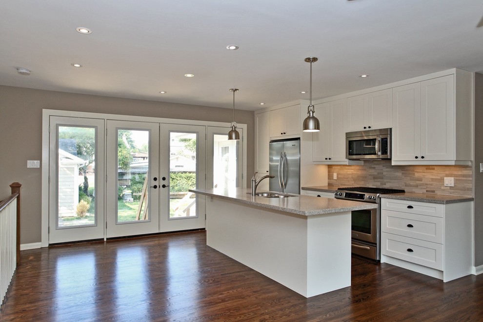 Example of a mid-sized transitional single-wall medium tone wood floor eat-in kitchen design in Toronto with a double-bowl sink, shaker cabinets, white cabinets, granite countertops, beige backsplash, stone tile backsplash, stainless steel appliances and an island