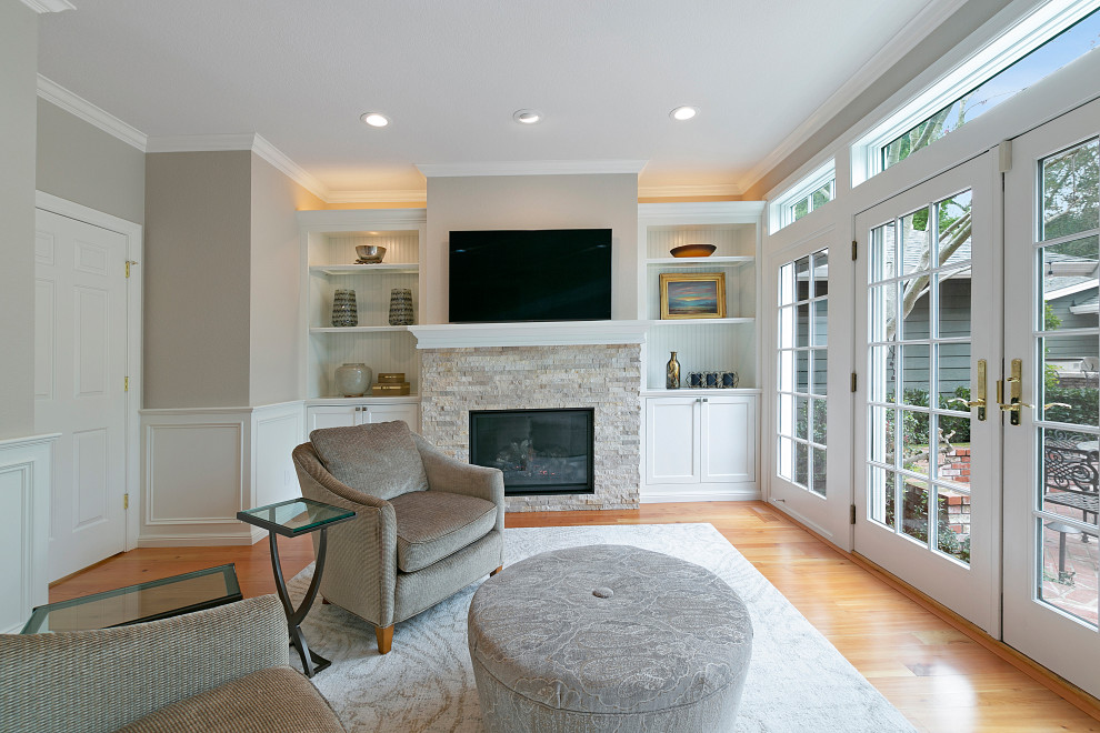 На фото: изолированная гостиная комната среднего размера в стиле неоклассика (современная классика) с серыми стенами, паркетным полом среднего тона, стандартным камином, фасадом камина из каменной кладки, коричневым полом и телевизором на стене с
