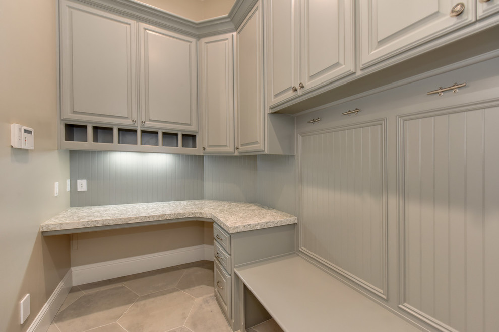 This is an example of a large traditional u-shaped dedicated laundry room in Sacramento with an undermount sink, raised-panel cabinets, grey cabinets, granite benchtops, beige walls, concrete floors, a side-by-side washer and dryer, brown floor and beige benchtop.