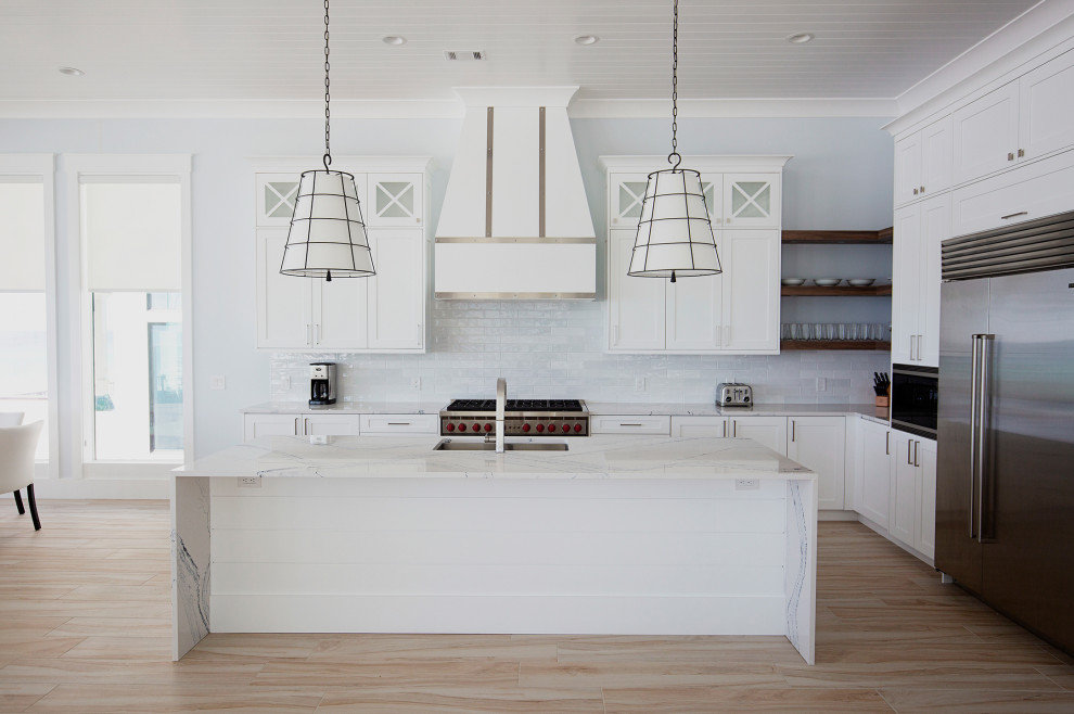 Example of a large beach style l-shaped medium tone wood floor and beige floor eat-in kitchen design in Miami with a drop-in sink, shaker cabinets, white cabinets, quartz countertops, white backsplash, ceramic backsplash, stainless steel appliances, an island and white countertops