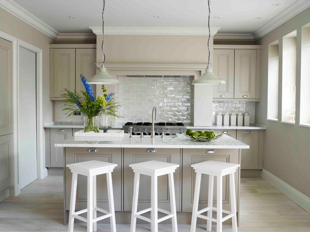 Design ideas for a mid-sized transitional galley open plan kitchen in London with beige cabinets, marble benchtops, white splashback, ceramic splashback, stainless steel appliances, light hardwood floors, with island, a farmhouse sink, recessed-panel cabinets and beige floor.