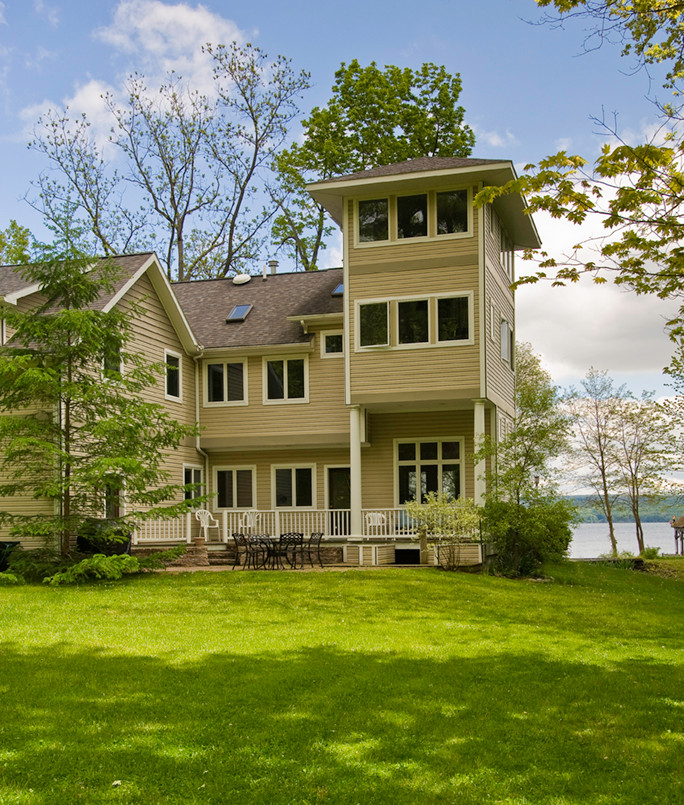 This is an example of a mid-sized transitional three-storey beige house exterior in New York with vinyl siding, a hip roof and a shingle roof.