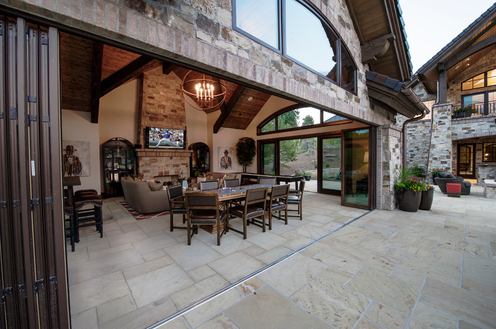 Photo of an expansive country enclosed family room in Denver with a game room, a wall-mounted tv, beige walls, limestone floors, a standard fireplace, a stone fireplace surround and white floor.