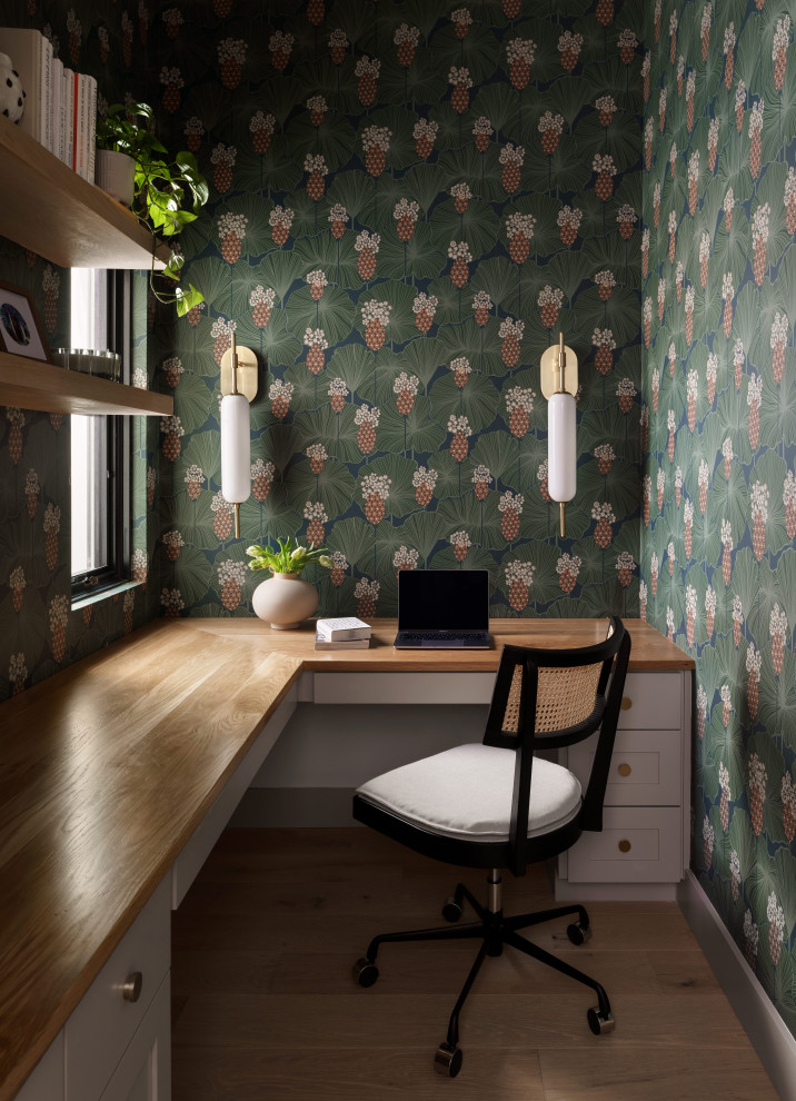 Traditional home office in Austin with green walls, medium hardwood flooring, a built-in desk, brown floors and wallpapered walls.