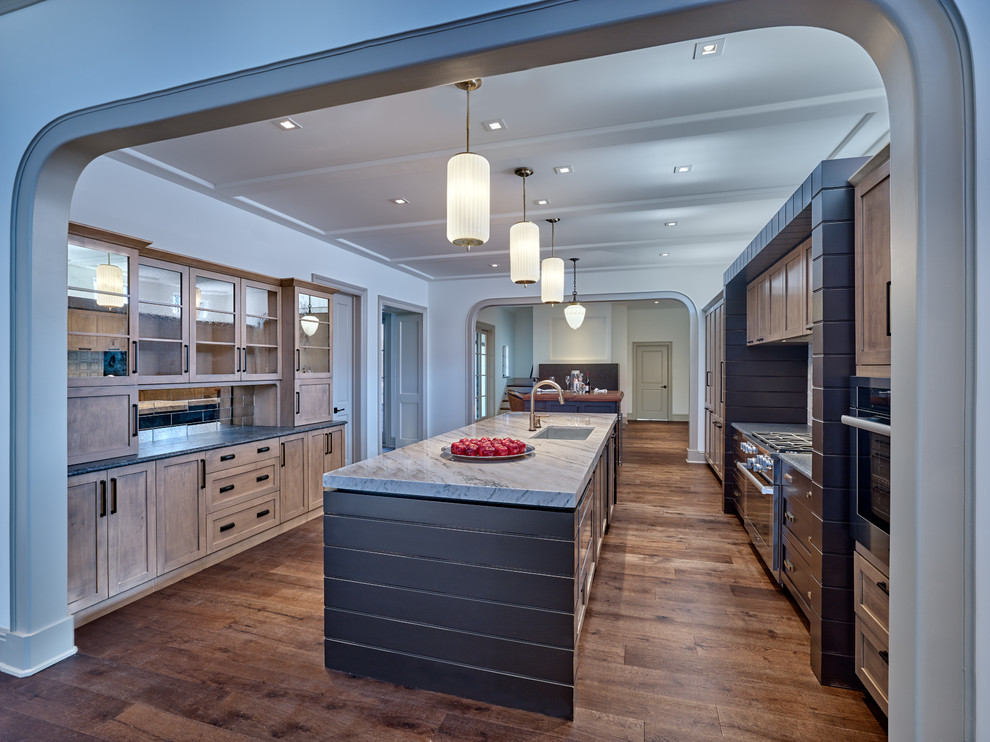 Photo of a large country single-wall kitchen in Philadelphia with a farmhouse sink, shaker cabinets, medium wood cabinets, quartzite benchtops, white splashback, marble splashback, stainless steel appliances, medium hardwood floors, multiple islands, brown floor and white benchtop.