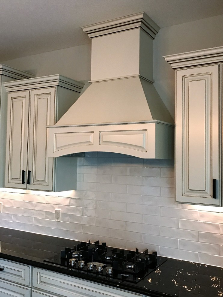 Inspiration for a large traditional l-shaped eat-in kitchen in Milwaukee with a drop-in sink, solid surface benchtops, white splashback, ceramic splashback, black appliances, with island and black benchtop.