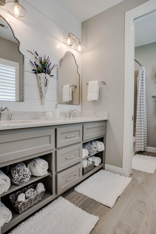 This is an example of a mid-sized traditional bathroom in Dallas with recessed-panel cabinets, grey cabinets, an alcove tub, a curbless shower, a two-piece toilet, gray tile, porcelain tile, grey walls, porcelain floors, an undermount sink, engineered quartz benchtops, grey floor, a hinged shower door and white benchtops.