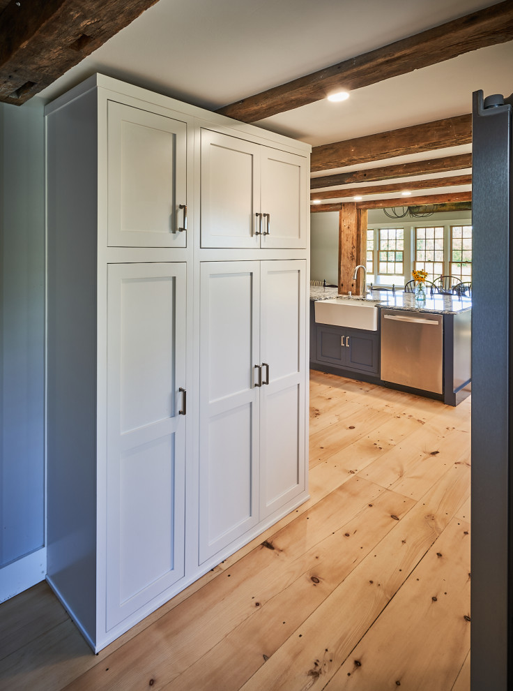 This is an example of a farmhouse kitchen/diner in Boston with a belfast sink, shaker cabinets, white cabinets, engineered stone countertops, white splashback, metro tiled splashback, stainless steel appliances, light hardwood flooring, an island, brown floors, blue worktops and exposed beams.