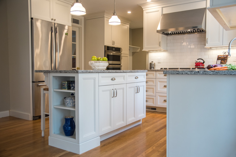Eat-in kitchen - mid-sized transitional l-shaped medium tone wood floor eat-in kitchen idea in Boston with a farmhouse sink, shaker cabinets, white cabinets, quartz countertops, white backsplash, subway tile backsplash, stainless steel appliances and an island