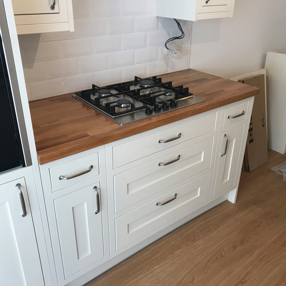 This is an example of a large traditional single-wall open plan kitchen in London with a single-bowl sink, shaker cabinets, white cabinets, wood benchtops, linoleum floors and multi-coloured benchtop.