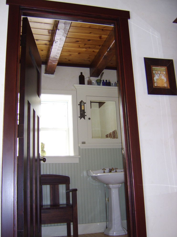 Photo of a mid-sized country powder room in Other with recessed-panel cabinets, white cabinets, white walls, medium hardwood floors and a pedestal sink.