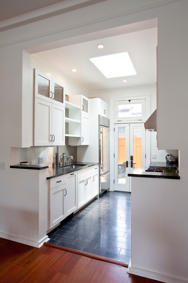 Photo of a contemporary galley kitchen in New Orleans with an undermount sink, shaker cabinets, white cabinets, metal splashback, stainless steel appliances and black floor.